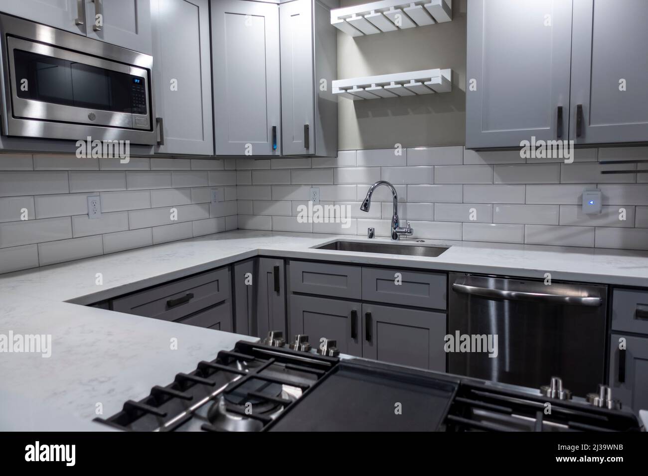 Abgewinkelte Ansicht einer weißen, leeren Küche mit Marmorplatten und einem Gasherd, der Wasserhahn im Hintergrund Stockfoto