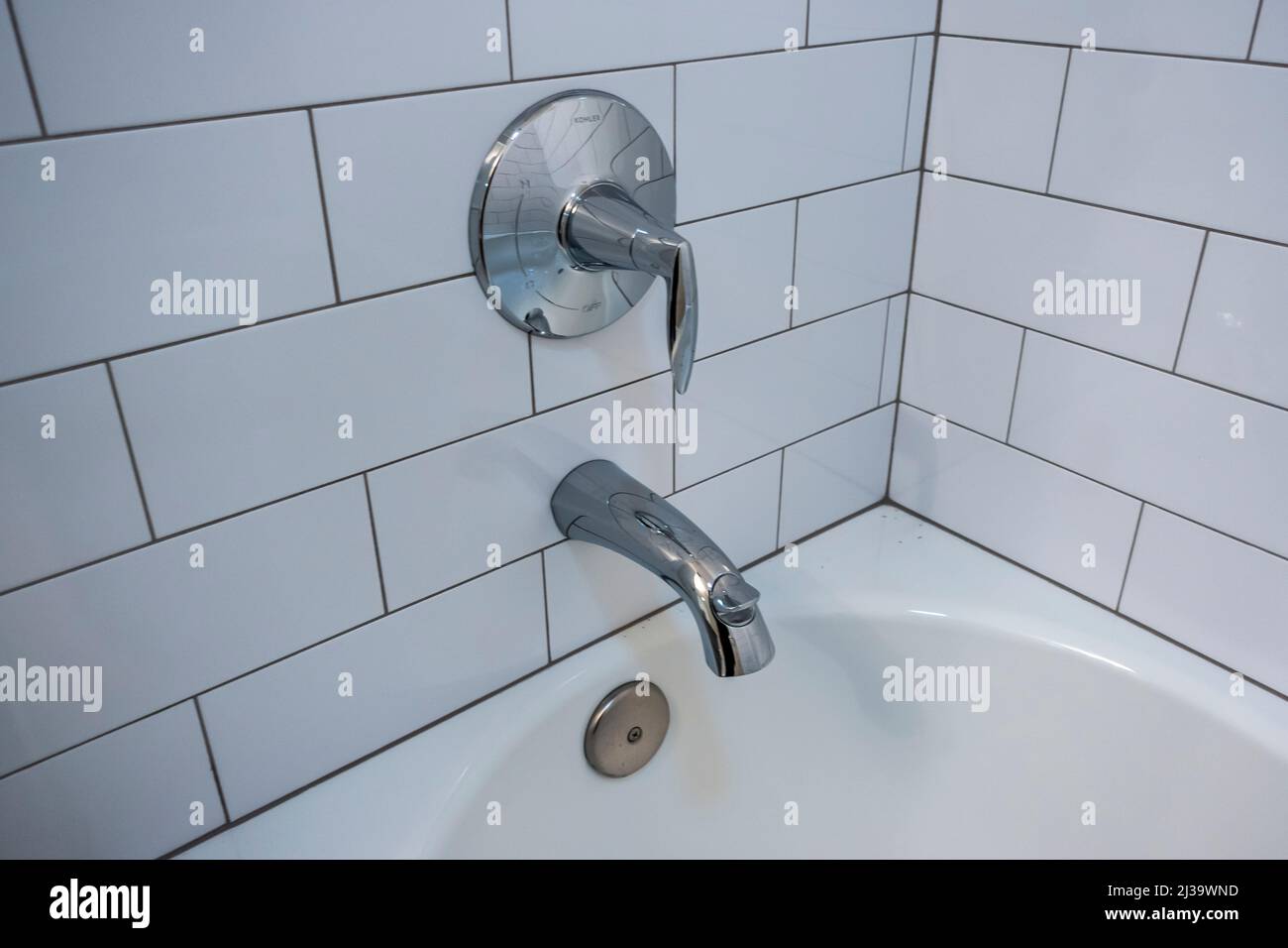 Blick auf eine silberne Badewanne mit Duschvorrichtung in einem weiß gefliesten Badezimmer Stockfoto