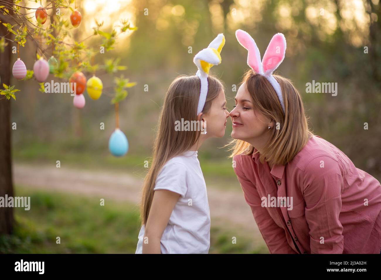 Schöne und glückliche Mutter und Tochter in Hasenohren schmücken den Baum mit ostereiern. Glückliche Familie feiert ostern. Stockfoto