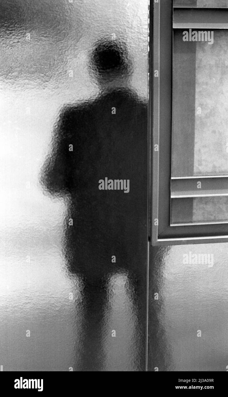 Diffuse Figur eines Mannes, der hinter abgeschrägtem Glas an einer Bushaltestelle in Paris, Frankreich, wartet Stockfoto