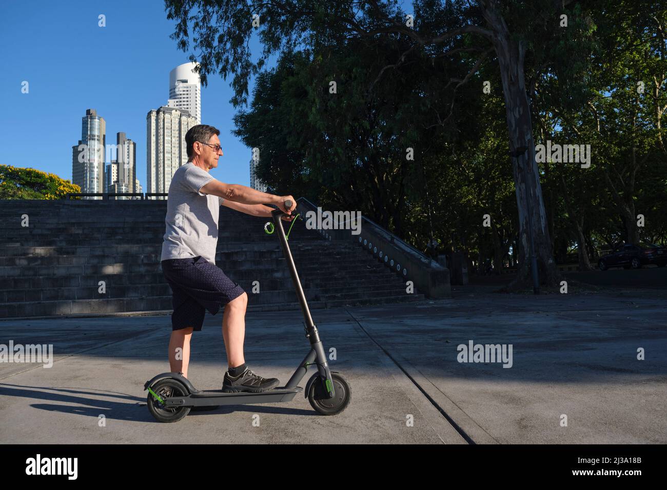 Hispanic Senior Mann mit seinem Elektro-Kick Scooter in der Stadt ein sonniger Morgen. Konzepte von Nachhaltigkeit, Modernität, aktivem Leben, sauberer Energie und g Stockfoto