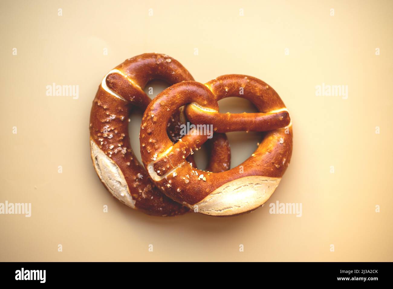 Zwei frisch gebackene Brezeln aus der Nähe, isoliert auf beigefarbenem Hintergrund. Stockfoto