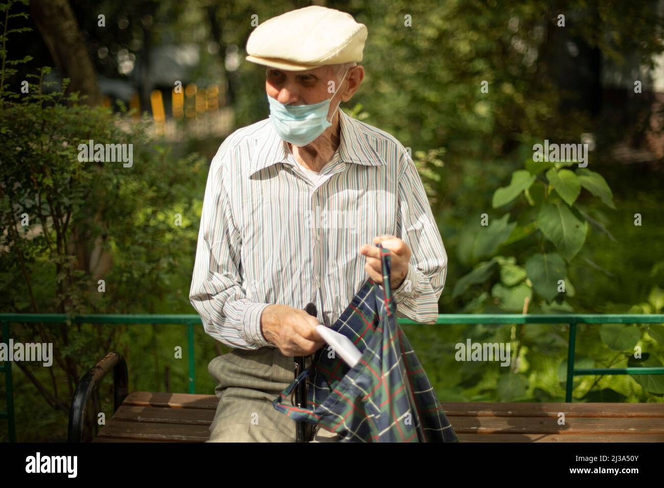 Der alte Mann sitzt im Sommer auf der Bank. Rentner in Russland in der Nähe  des Hauses. Mann mit medizinischer Maske. Opa in Hemd und Mütze  Stockfotografie - Alamy