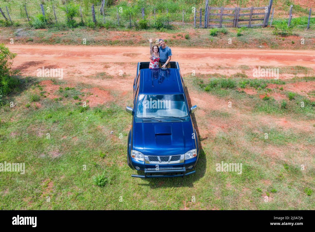 Luftaufnahme einer Frau und eines Mannes auf dem Rücken eines Pick-up-Trucks in Paraguay mit typisch rotem Sandweg. Stockfoto