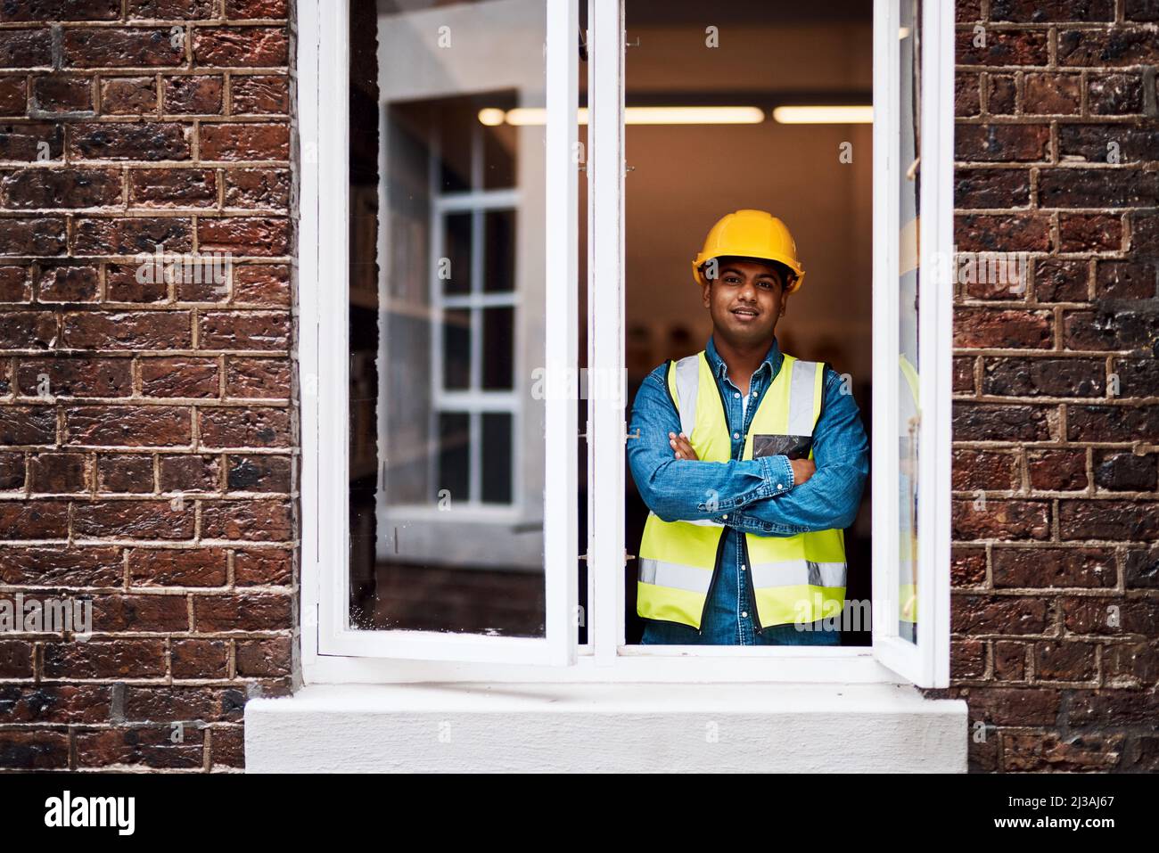Mein Team und ich werden dieses Gebäude umgestalten. Aufnahme eines jungen Ingenieurs, der im Fenster einer Baustelle steht. Stockfoto