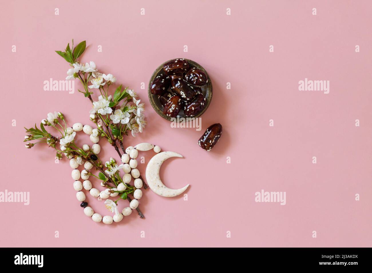 Ramadan-Konzept für Speisen und Getränke. Islamische Rosenkranzperlen, weiße Blumen und Datteln aus dem Ramadan auf einem hellrosa Hintergrund. Iftar-Abendessen. Draufsicht flach l Stockfoto