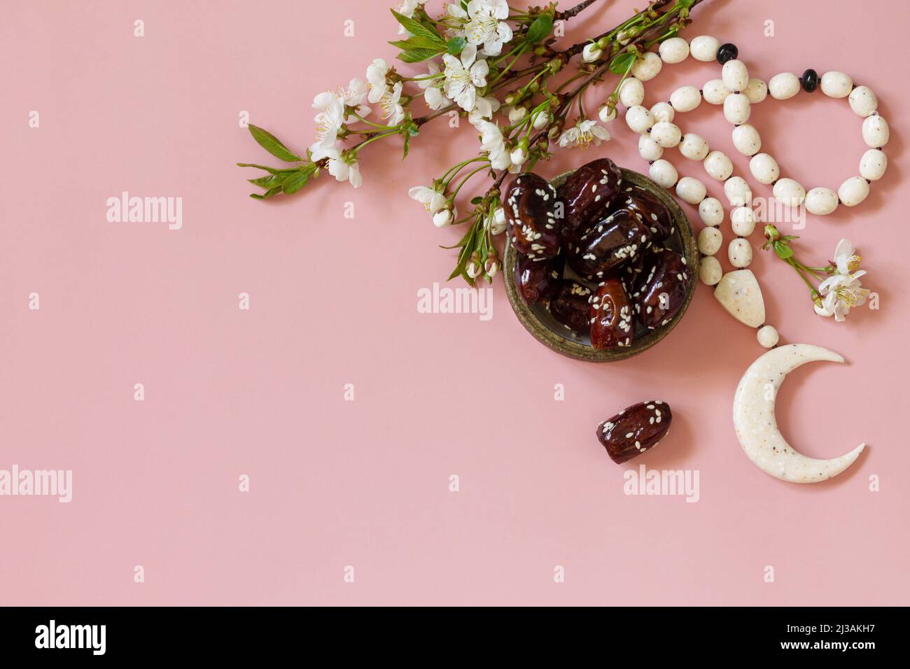 Ramadan-Konzept für Speisen und Getränke. Islamische Rosenkranzperlen, weiße Blumen und Datteln aus dem Ramadan auf einem hellrosa Hintergrund. Iftar-Abendessen. Draufsicht flach l Stockfoto