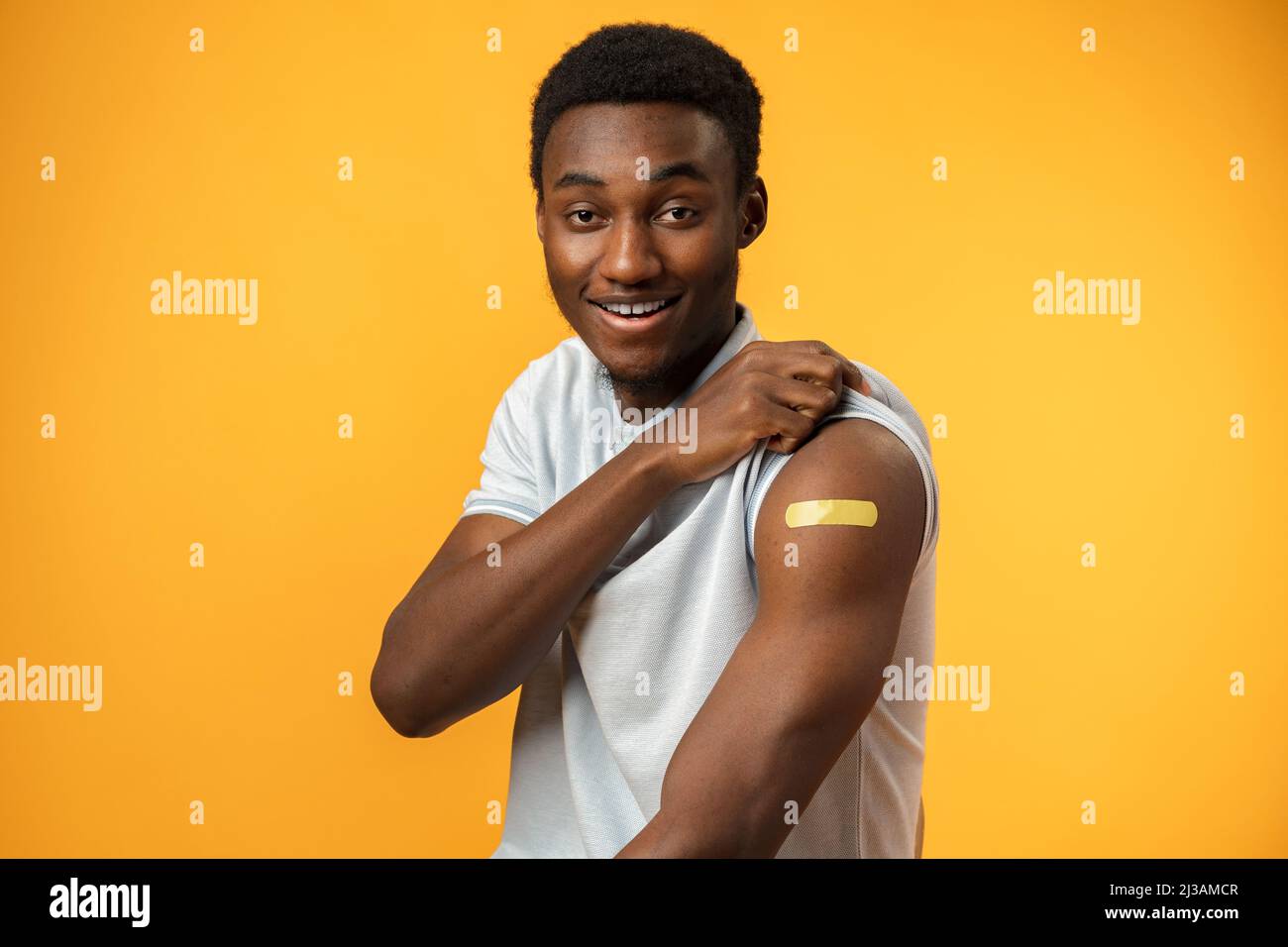 Geimpfter afroamerikanischer Mann, der seinen Arm vor gelbem Hintergrund zeigt Stockfoto