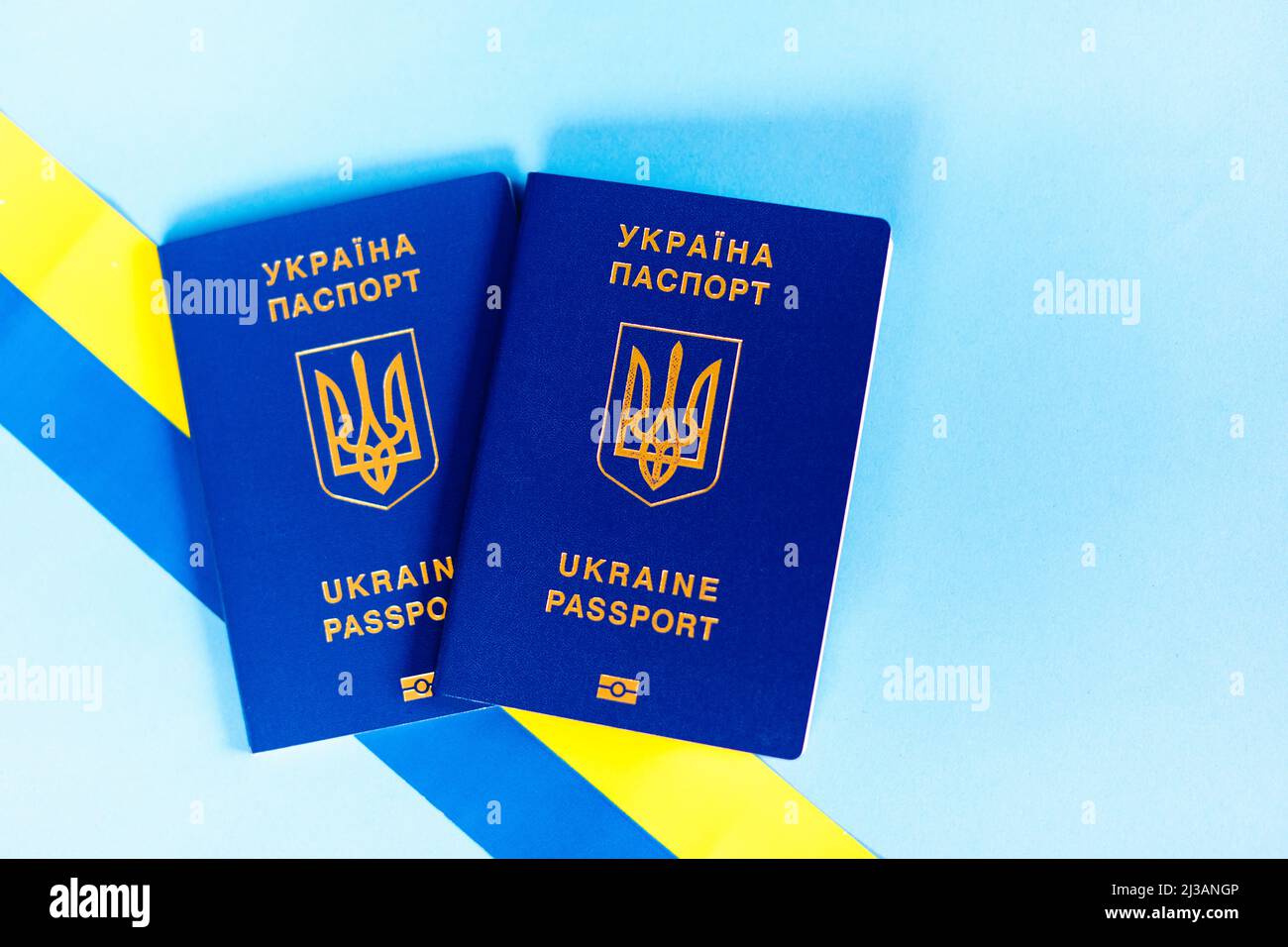 Zwei biometrische Pässe ukrainischer Staatsbürger auf blauem Hintergrund und mit einem gelben und blauen Band. Das Konzept der Migration der Ukrainer Stockfoto