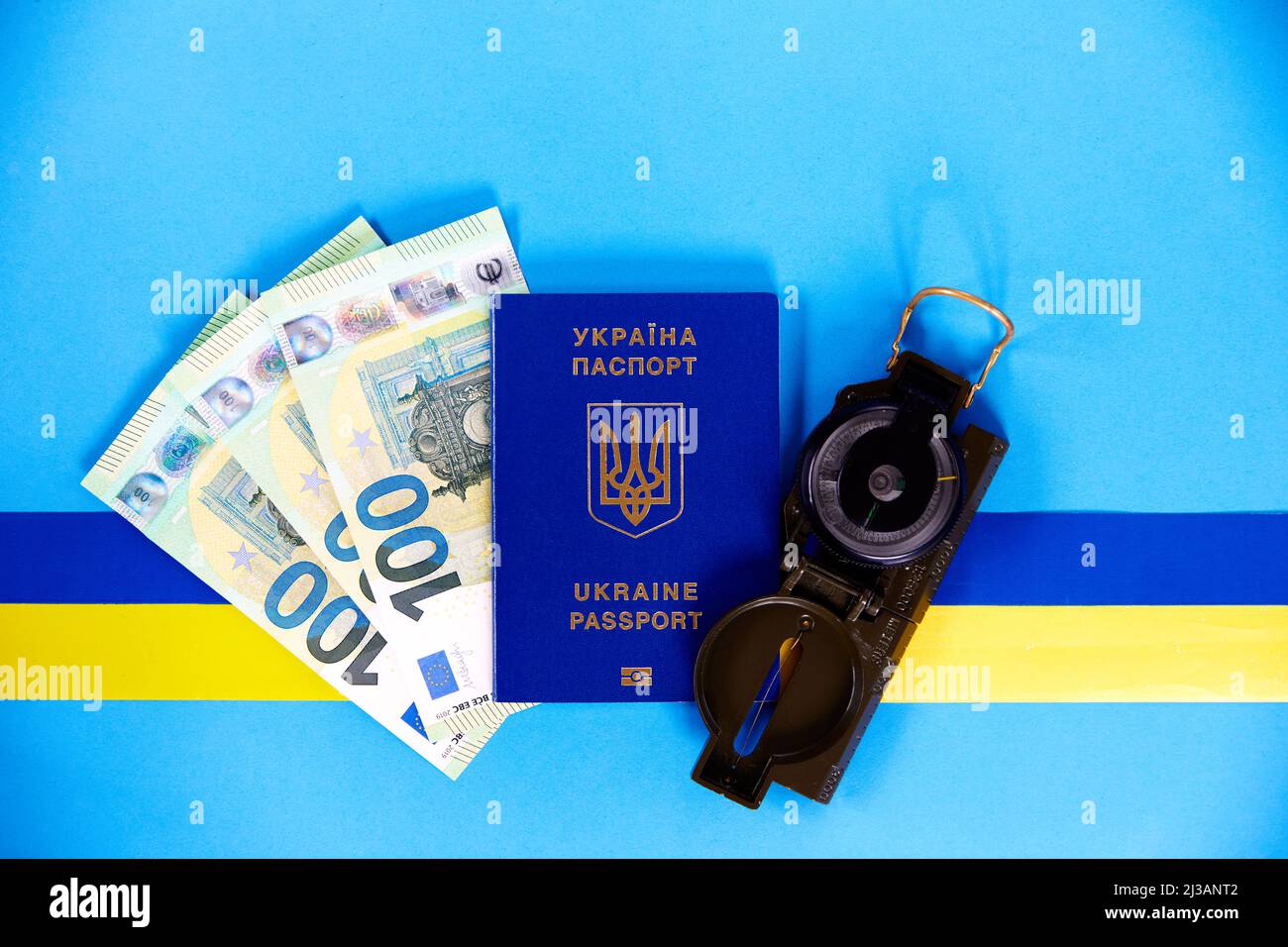 Zwei biometrische Pässe ukrainischer Bürger und Euro-Banknoten und Kompass auf blauem Hintergrund mit einem gelben und blauen Band. Das Konzept der Migrat Stockfoto