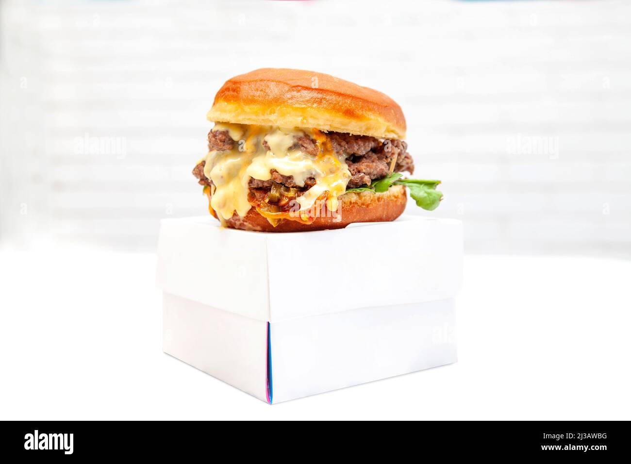 Double Decker Donut Bun Burger mit Rinderpasteten und Dressing auf einer Schachtel zum Mitnehmen. Stockfoto