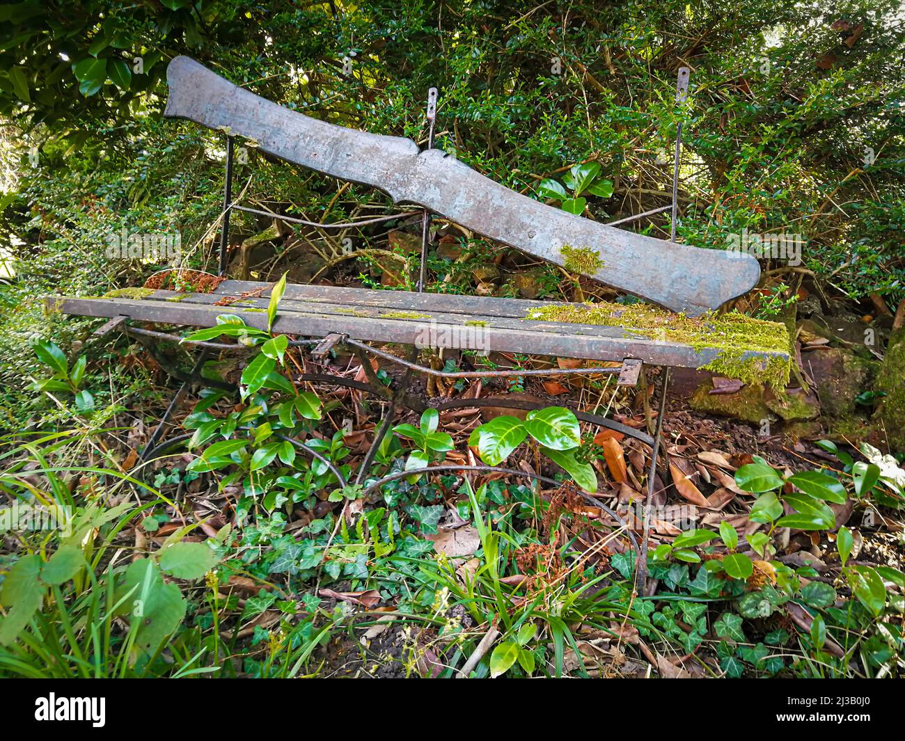Alte, reparaturbedürftige Holzbank, die in einem verlassenen Garten fast überwuchert ist Stockfoto