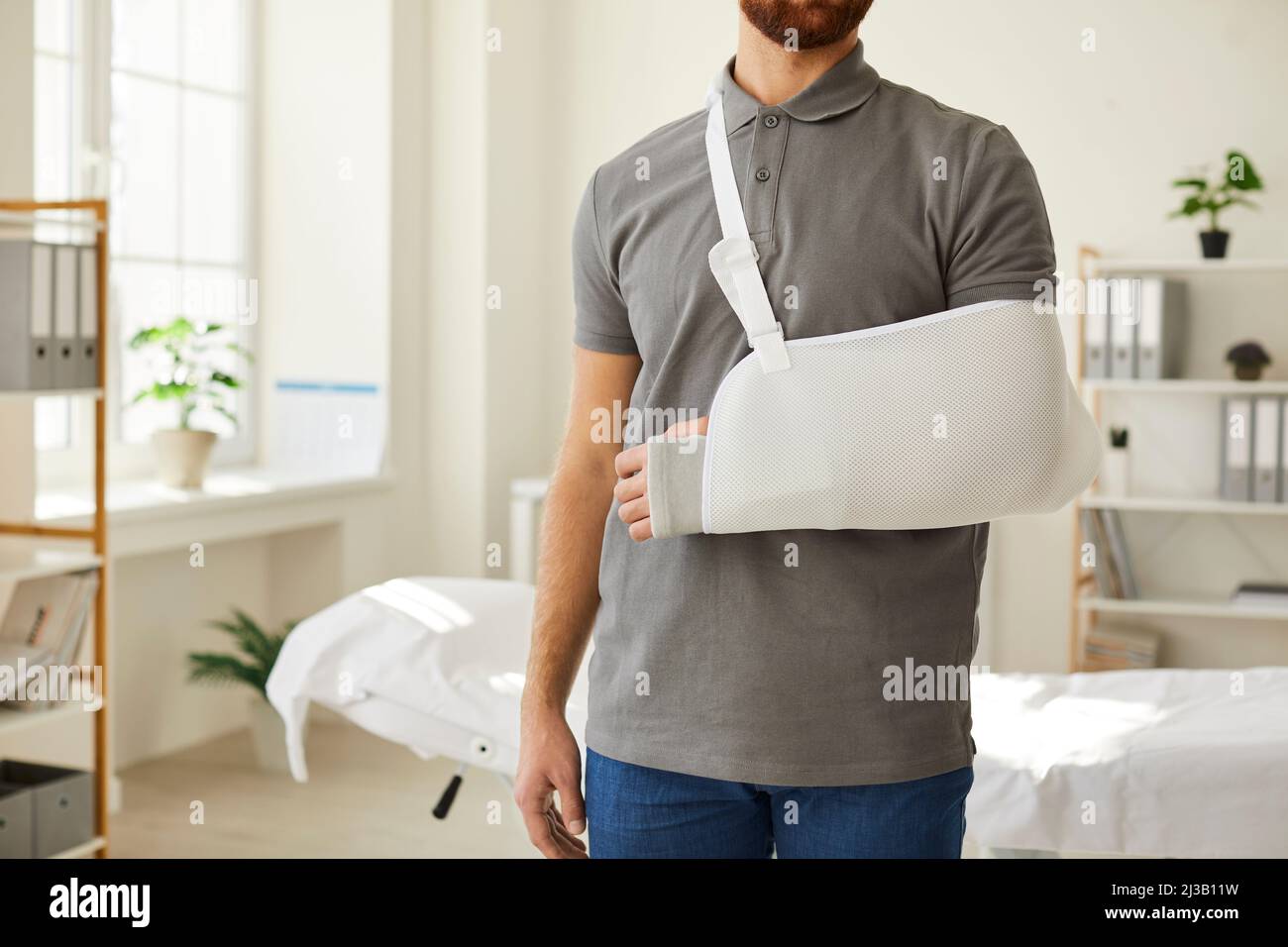 Unbekannter Mann, der am gebrochenen Arm eine Armbinde trägt, steht im medizinischen Büro. Stockfoto