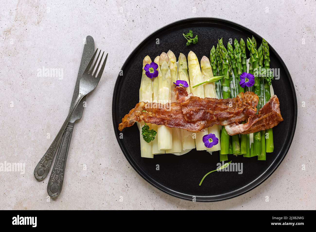 Grüner und weißer Spargel mit gebratenem Speck. Stockfoto