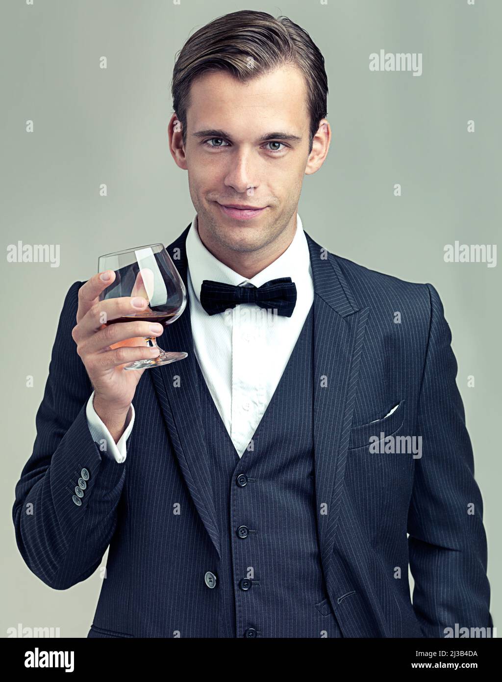 Heres to Frivolity. Ein Porträt eines eleganten jungen Mannes mit einem Glas Wein in einem Vintage-Anzug. Stockfoto