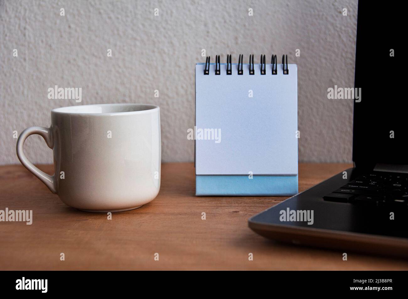 Leerer Notizblock mit Kaffeetasse und Laptop auf Holztisch. Speicherplatz kopieren Stockfoto