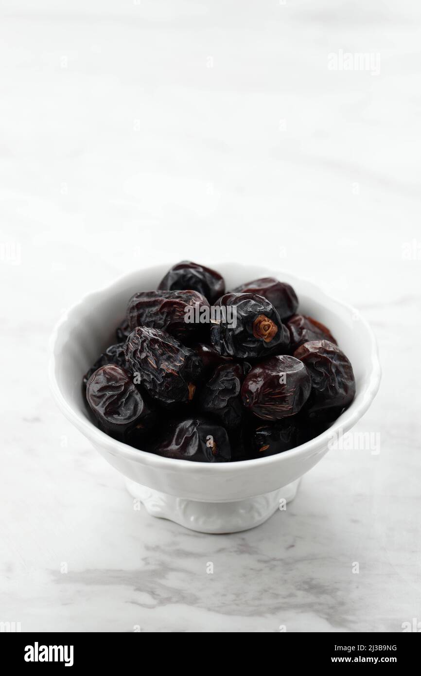 Ajwa Dates auf White Bowl, White Table. Aywa Date Fruit beliebt als Kurma Nabi, serviert für Ramadan Ifthar Stockfoto