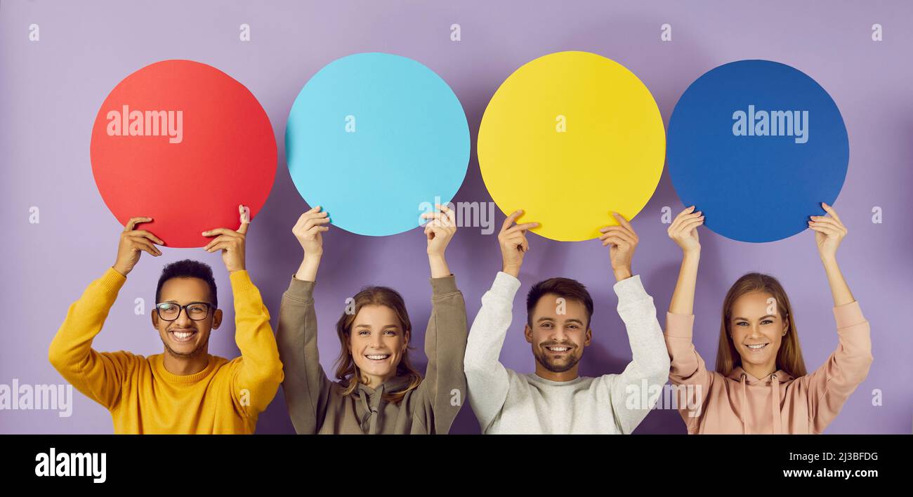 Farbige runde Sprechblasen mit Kopierraum in den Händen glücklicher junger Menschen auf violettem Hintergrund. Stockfoto
