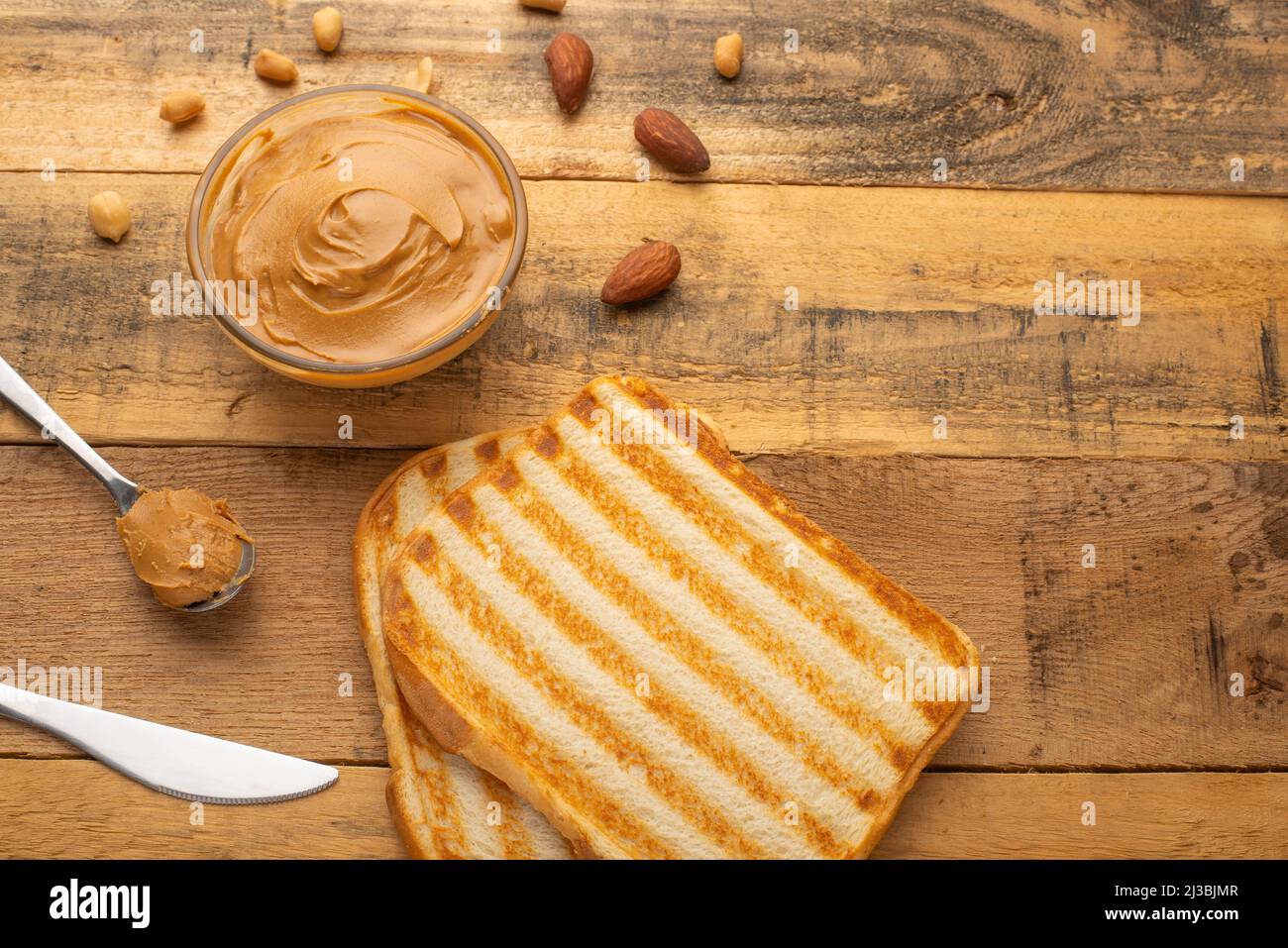 Erdnussbutter, Toast und Nüsse auf Holzstruktur, Draufsicht, Frühstück, leckeres und herzhaftes Essen Stockfoto