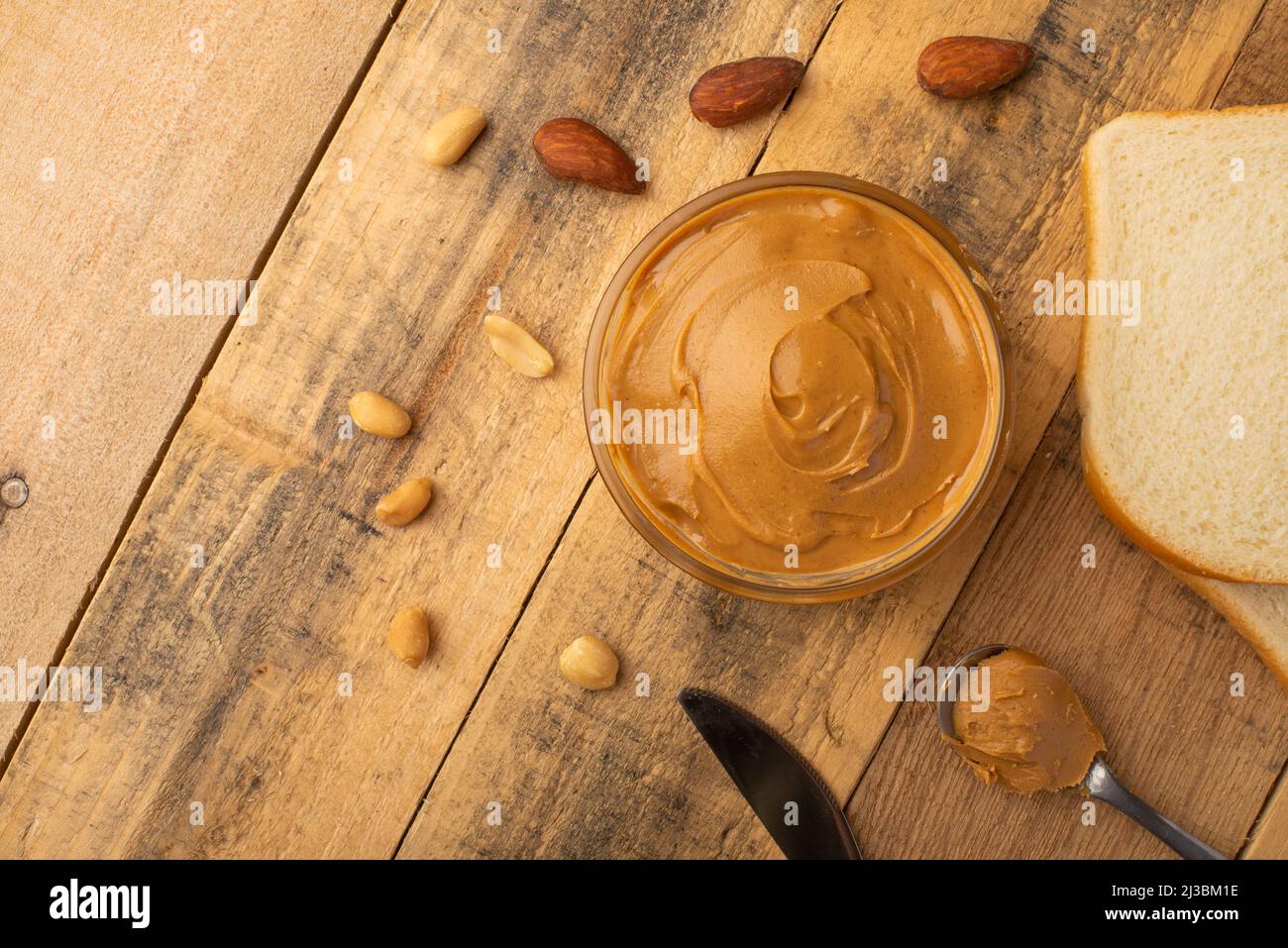 Schüsseln mit Erdnussbutter und Erdnüssen auf dunklem Holzboden aus der Sicht von oben, reichhaltiges Frühstück Stockfoto