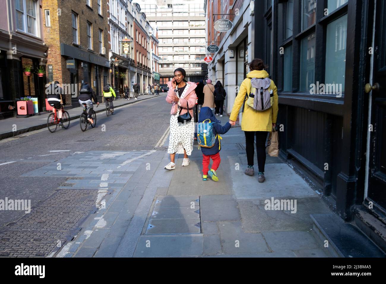 Rückansicht der Mutter mit der Hand des Kindes, die nach der Abholung von der Schule in City of London, Großbritannien, AUF der Straße nach Hause ging Stockfoto