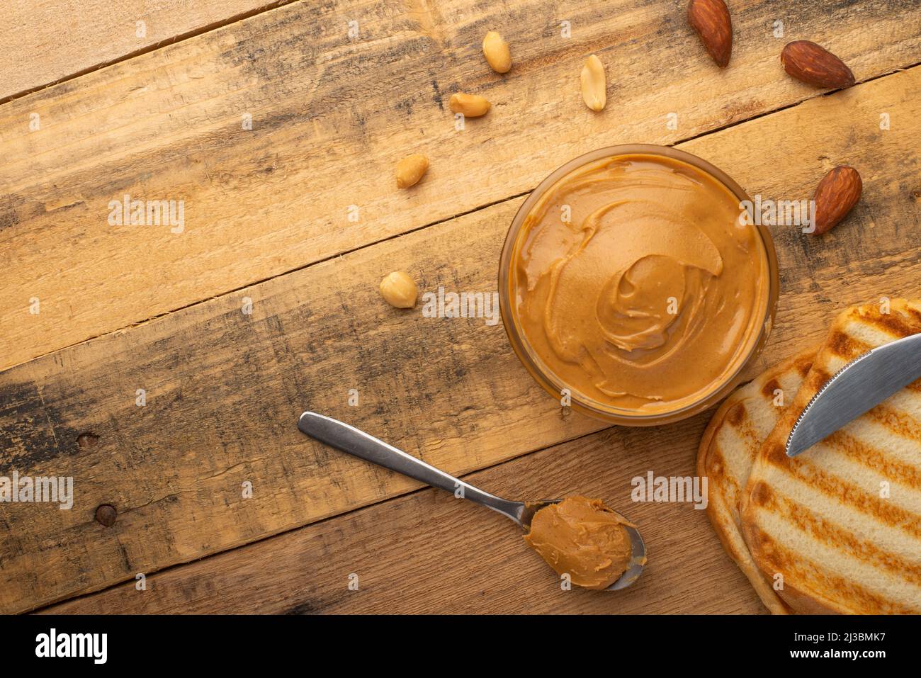 Schüsseln mit Erdnussbutter und Erdnüssen auf dunklem Holzboden aus der Sicht von oben, reichhaltiges Frühstück Stockfoto