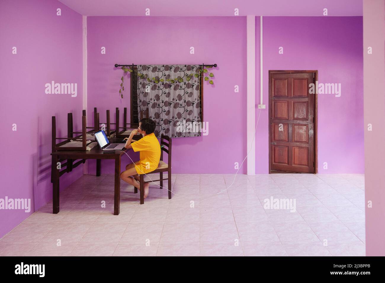 Junge benutzt Laptop in pinkem Zimmer Stockfoto