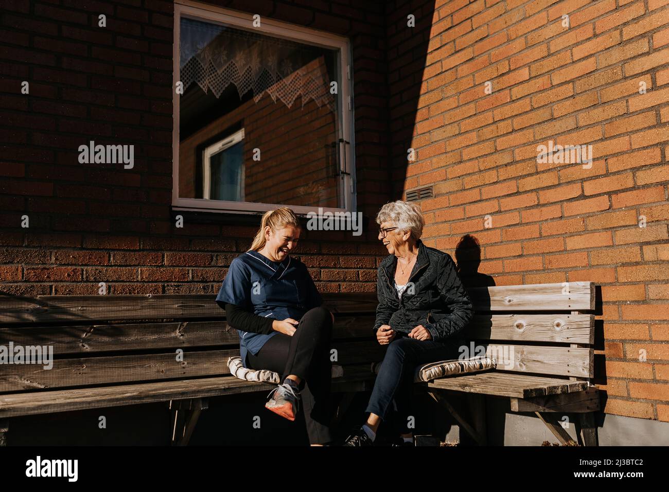 Hausmeisterin und ältere Frau sitzen auf der Bank und lachen Stockfoto