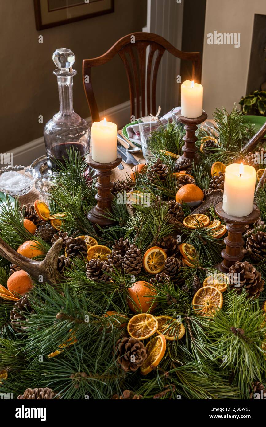 Zündete Kerzen mit aufgeschnittenem Orange und Pinecon-Mittelpunkt auf dem Esstisch zu Weihnachten in Suffolk Cottage aus dem 18.. Jahrhundert, Großbritannien Stockfoto
