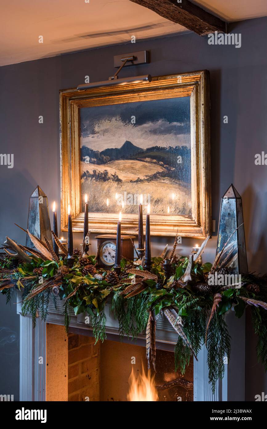 Feenfedern und brennende Kerzen mit goldgerahmter Landschaftsmalerei auf Mantelpiece in Suffolk Cottage aus dem 18.. Jahrhundert zu Weihnachten, Großbritannien Stockfoto