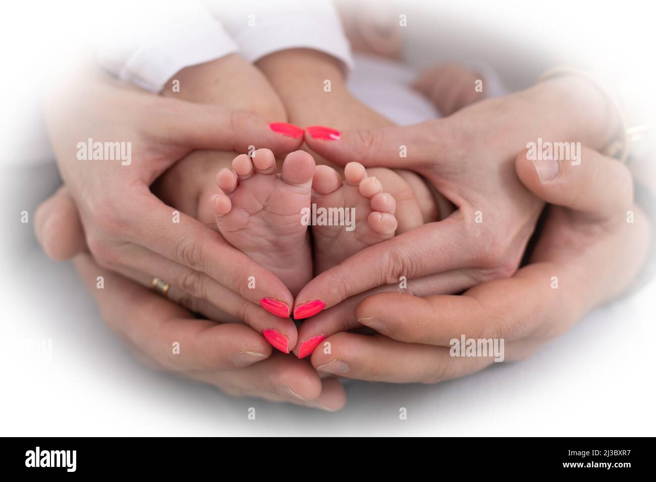 Junge unkenntliche Familie von Mutter Vater und Kind. Mama, Papa halten die Beine, der Fuß des Neugeborenen in den Handflächen Stockfoto