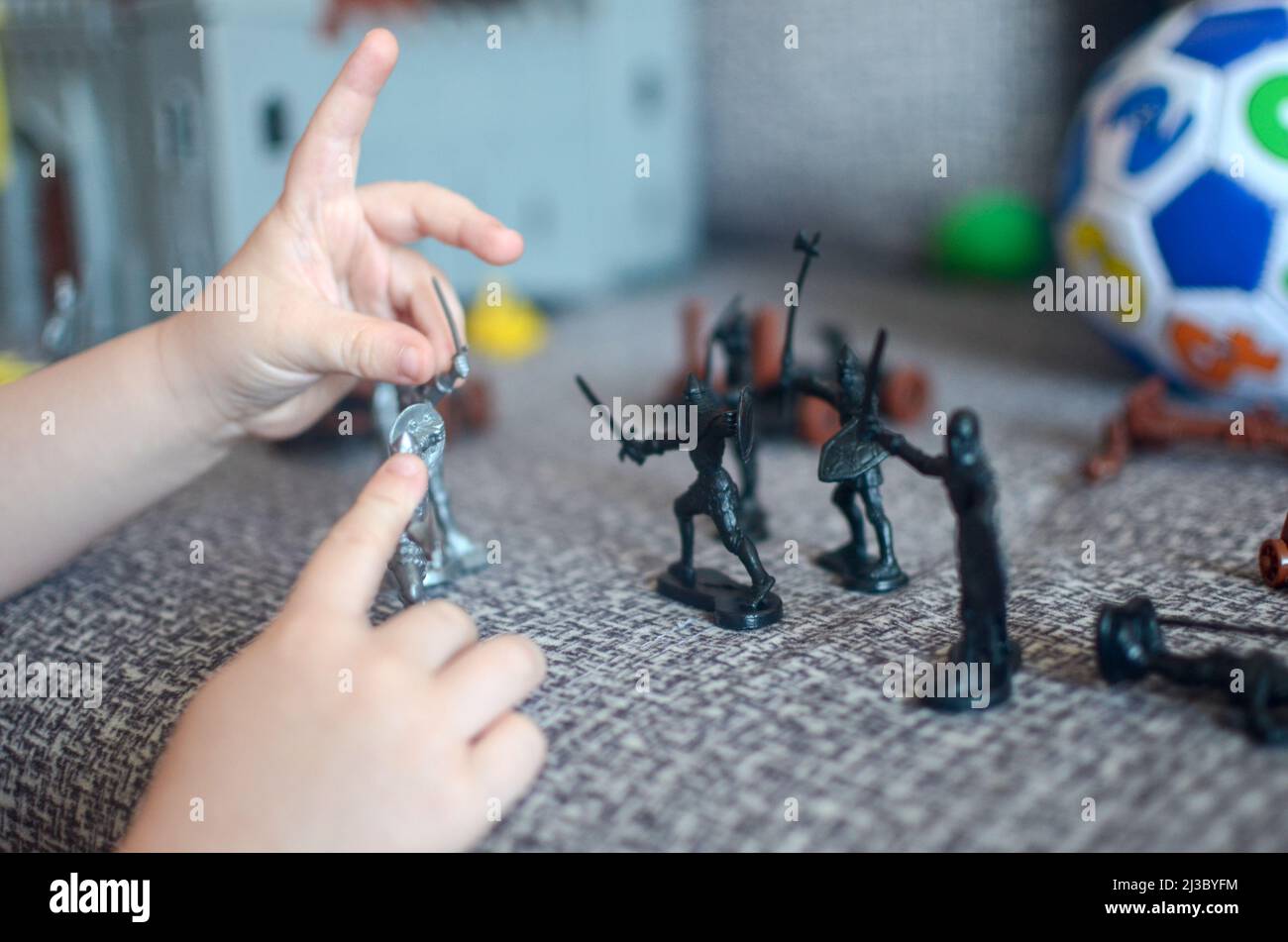 Home Spiele für Vorschulkinder Konzept - Jungen Hände spielen Spielzeug Soldaten auf einem gesichtslosen Sofa vor dem Hintergrund einer Burg und einem Ball. Stockfoto