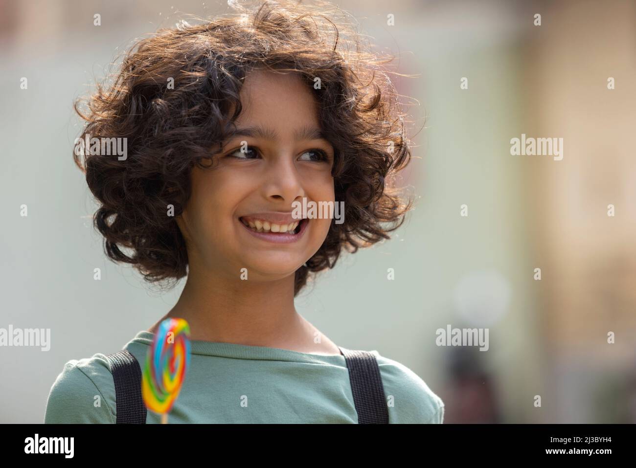 Porträt eines Jungen, der einen bunten großen Lutscher in der Hand hält und sich anderswo umsieht Stockfoto