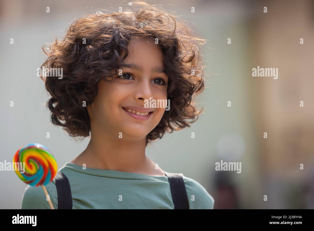 Porträt eines Jungen, der einen bunten großen Lutscher in der Hand hält und sich anderswo umsieht Stockfoto