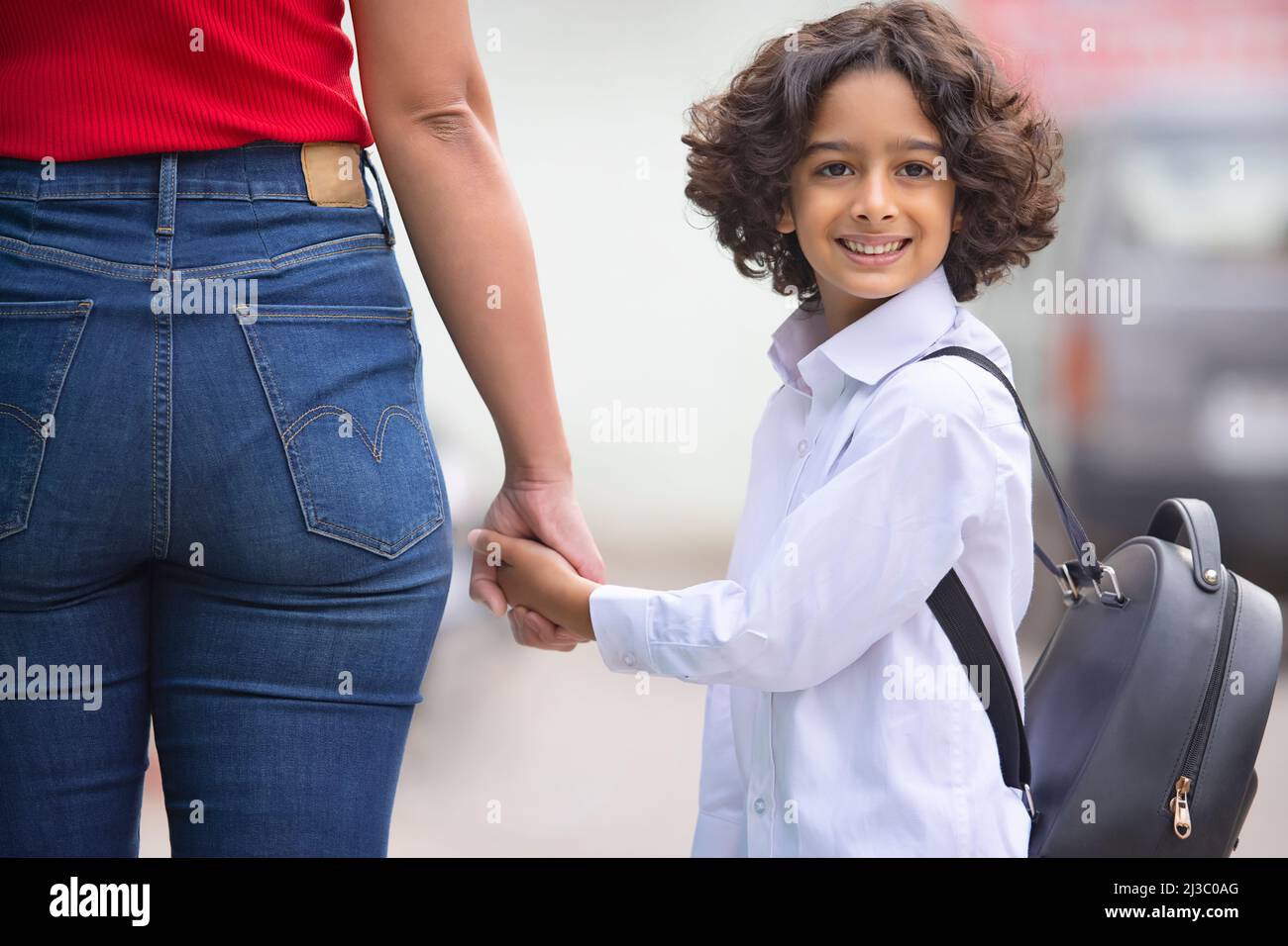 Porträt eines Schuljungen, der die Hand hält und lächelnd zurückblickt Stockfoto