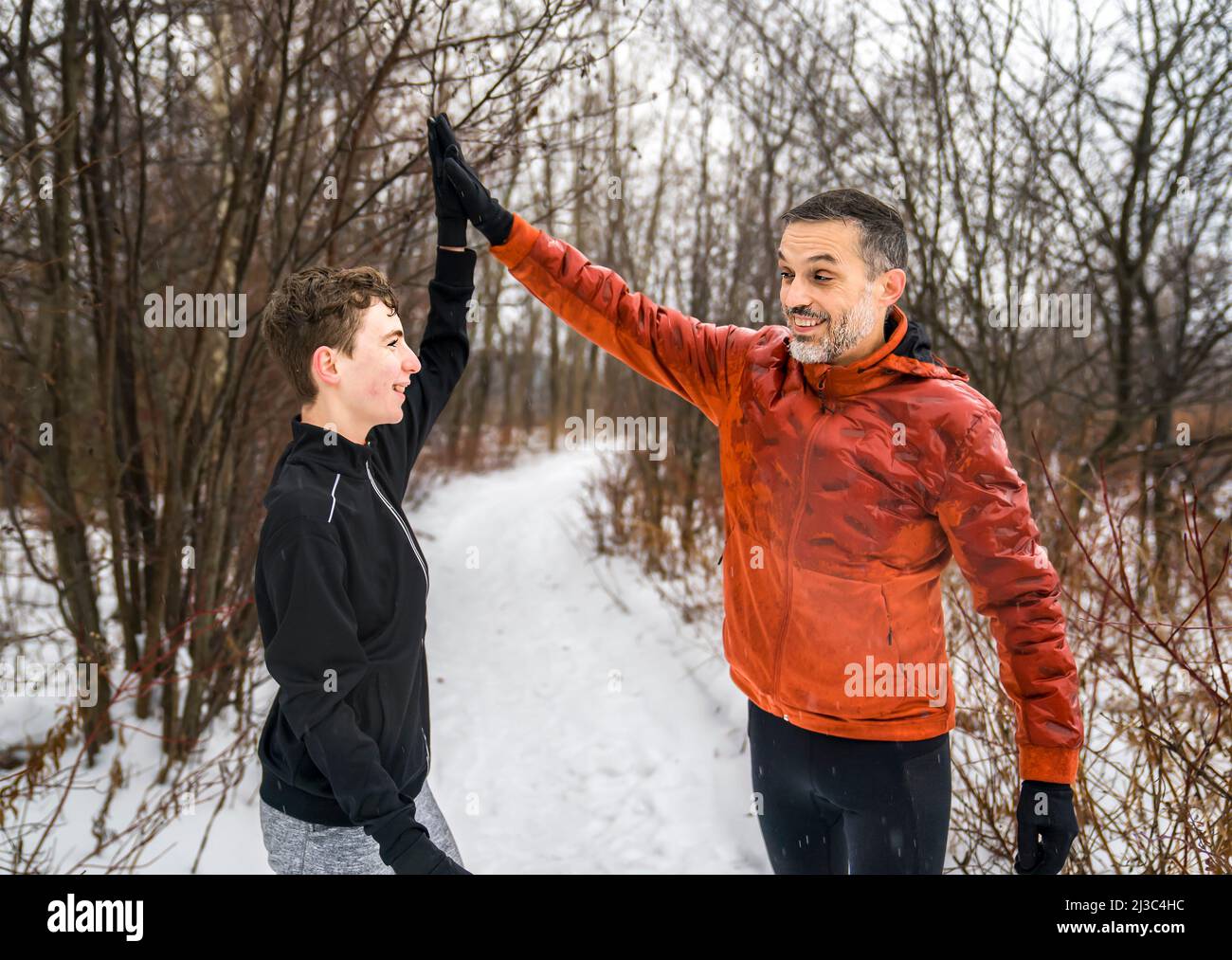 Vater mit Sohn Sport läuft zusammen draußen in der Wintersaison tun High Five Stockfoto