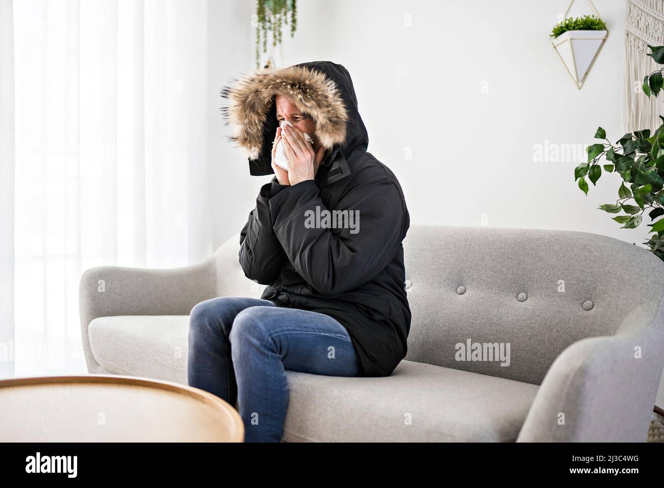 Mann mit warmer Kleidung das Gefühl der Kälte im Haus auf dem Sofa blasen die Nase Stockfoto