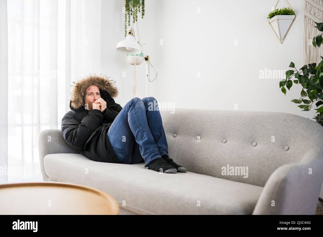Mann mit warmer Kleidung das Gefühl der Kälte im Haus auf dem Sofa blasen die Nase Stockfoto