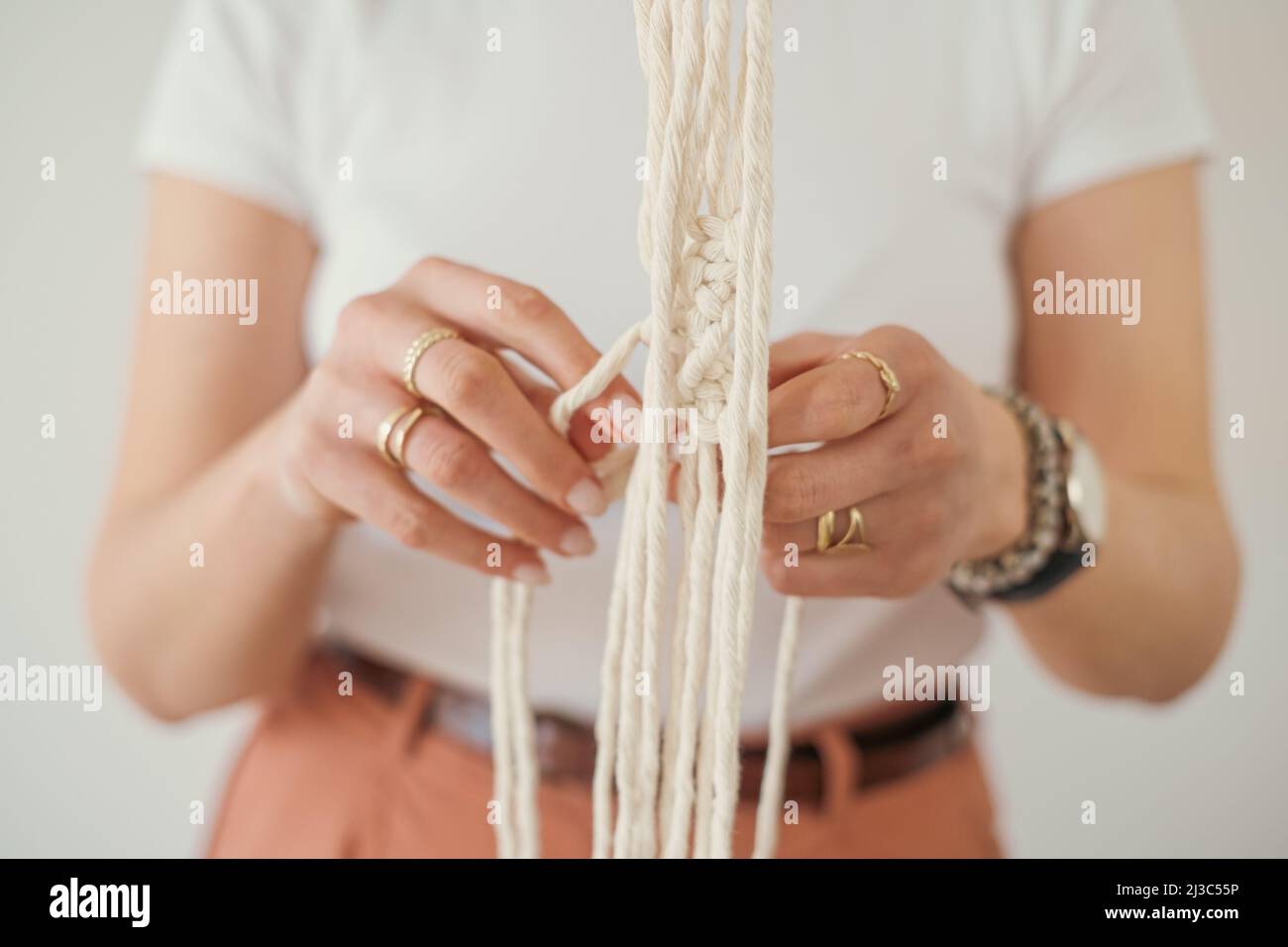 Damenhände weben einen Blumentopfhalter im Macrame-Muster im Boho-Stil. Stockfoto