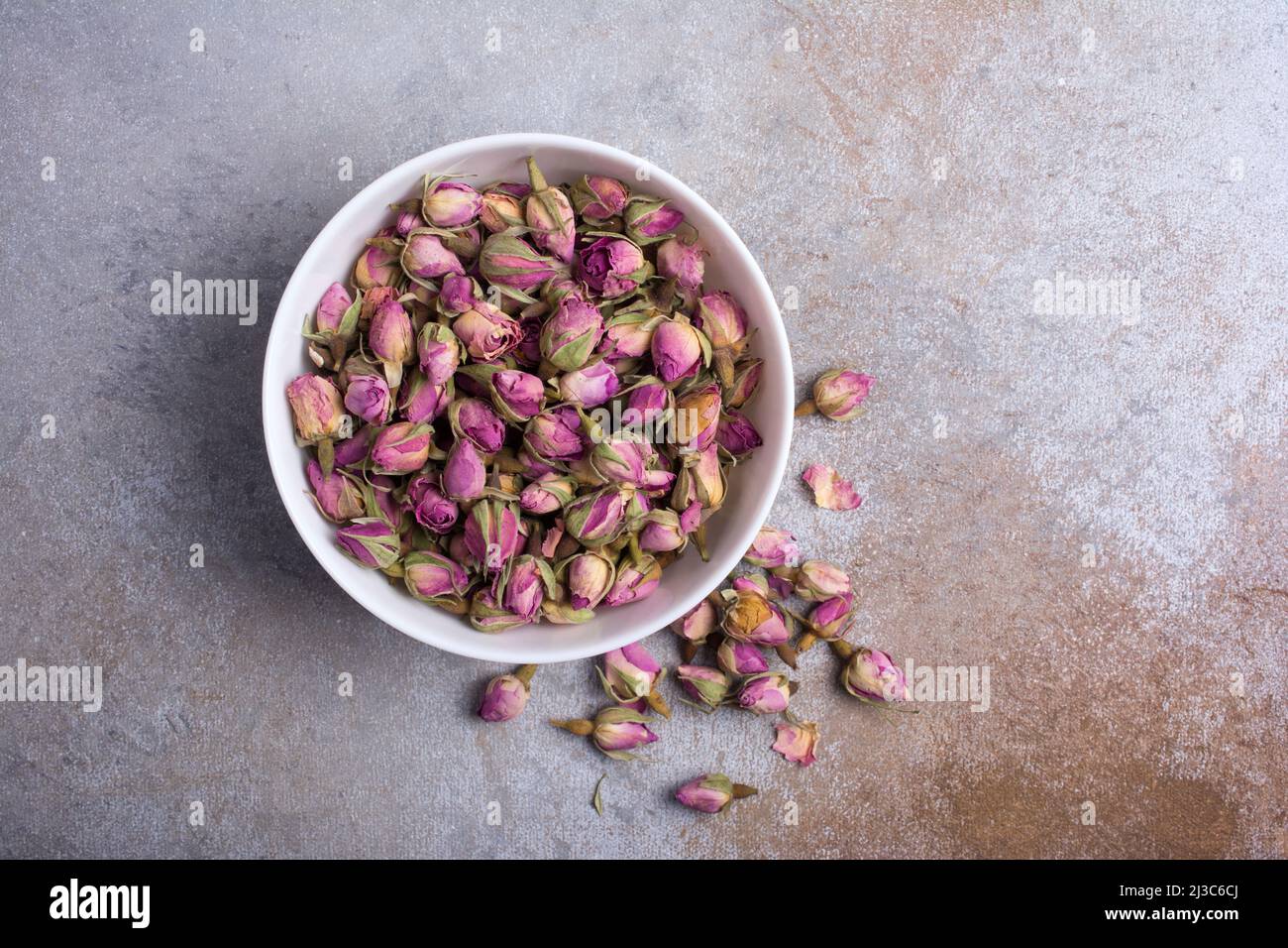 Draufsicht auf weiße Schale mit getrockneten Rosenknospen für duftenden Tee auf grauem Betongrund Stockfoto