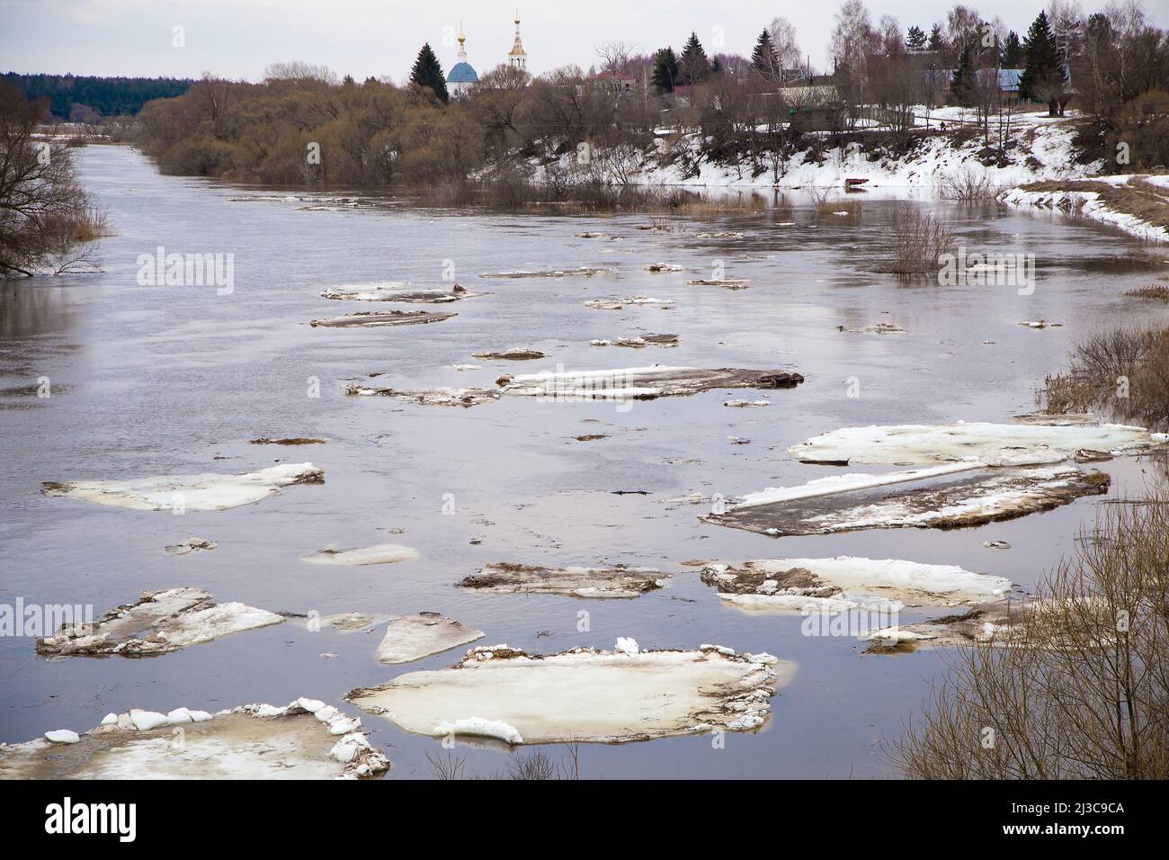 Eine Gruppe großer weißer Eisschollen schwimmt den Fluss hinunter. Frühling, Schnee schmilzt, trockenes Gras rundherum, Überschwemmungen beginnen und der Fluss überfließt. Tag, bewölktes Wetter, weiches warmes Licht. Stockfoto