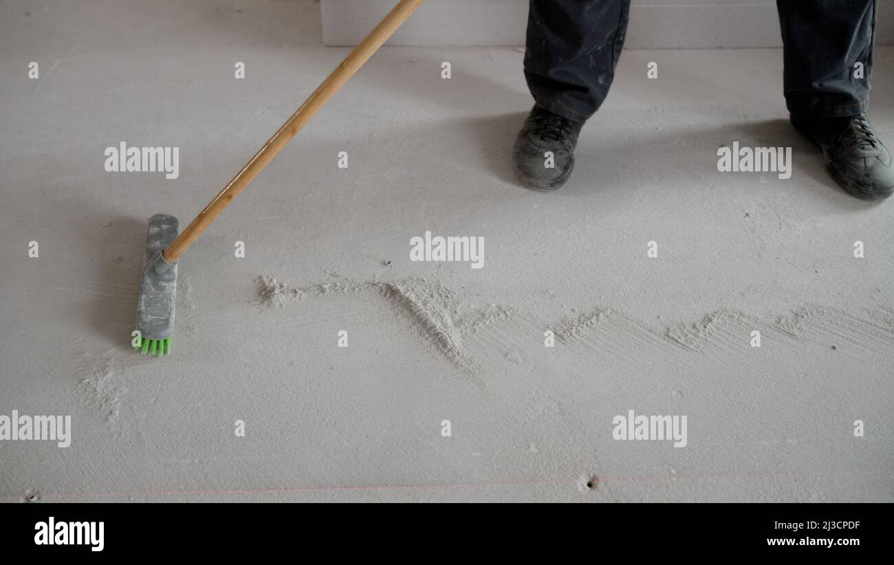 Nach der Reparatur bürstet ein Arbeiter den Boden. Ein Arbeiter fegt weißen Betonstaub vom Boden. Müllabfuhr nach Reparaturarbeiten zu Hause. Stockfoto