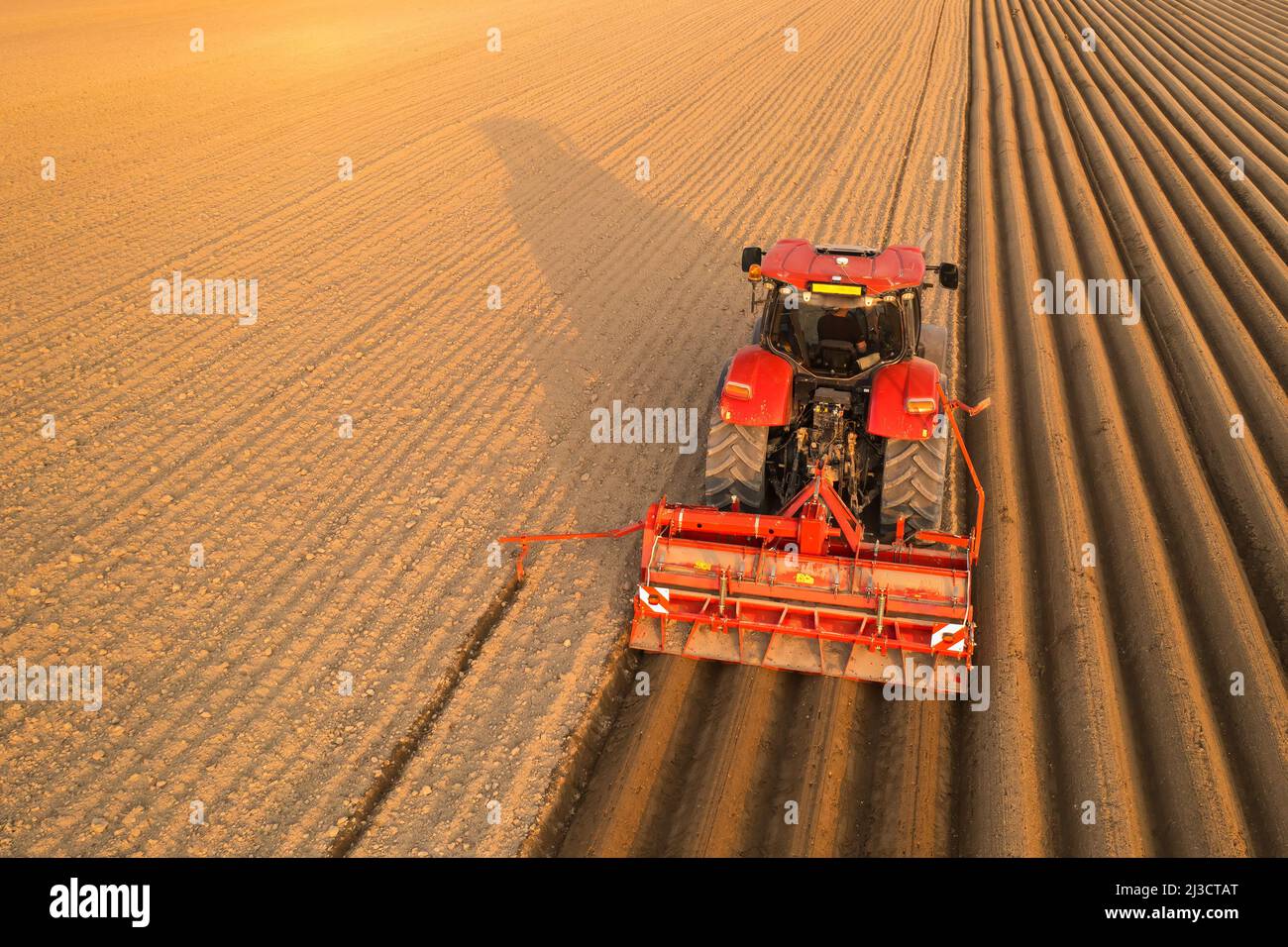 Traktor schleppt Pflug, um lange Furchen im Boden an sonnigen Tag zu hinterlassen. Landwirtschaftliche Transportarbeiten in endlosen Feld bei Sonnenuntergang Luftaufnahme Stockfoto