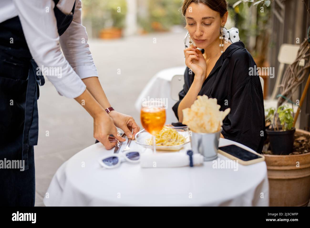 Kellner serviert Tisch für eine junge Kundin im Freien Stockfoto