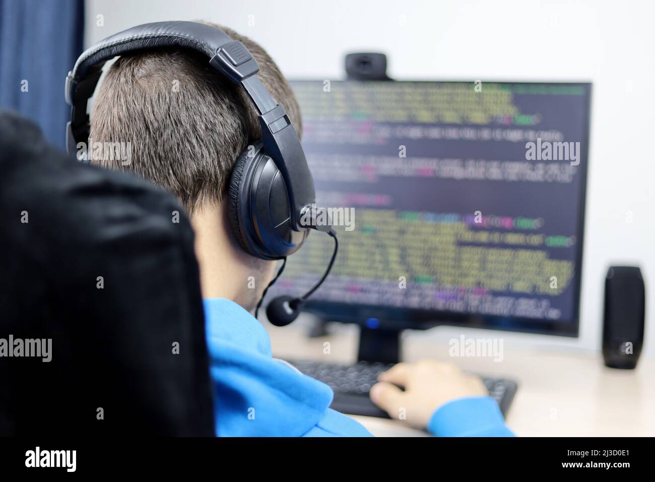 Programmierung, Cyberkriminalität und Hacking. Nicht erkennbarer Typ in Kopfhörern, der am Desktop-PC sitzt und den Standort- oder Anwendungscode auf dem Monitor hat Stockfoto