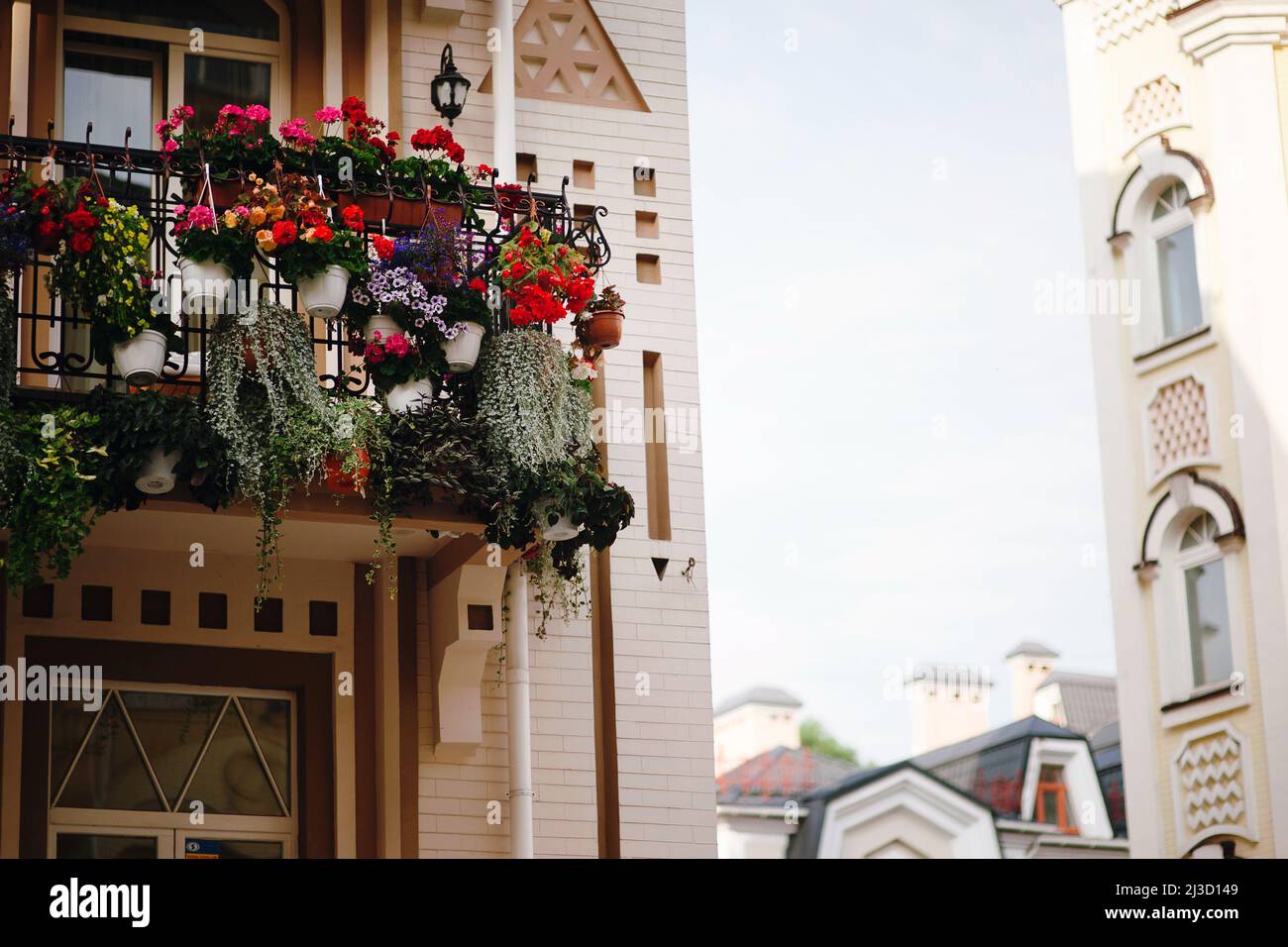 Quarantänezeit. Weißes Gebäude mit schönen, hellen Blumen auf dem Balkon und frischem Grün. Stockfoto