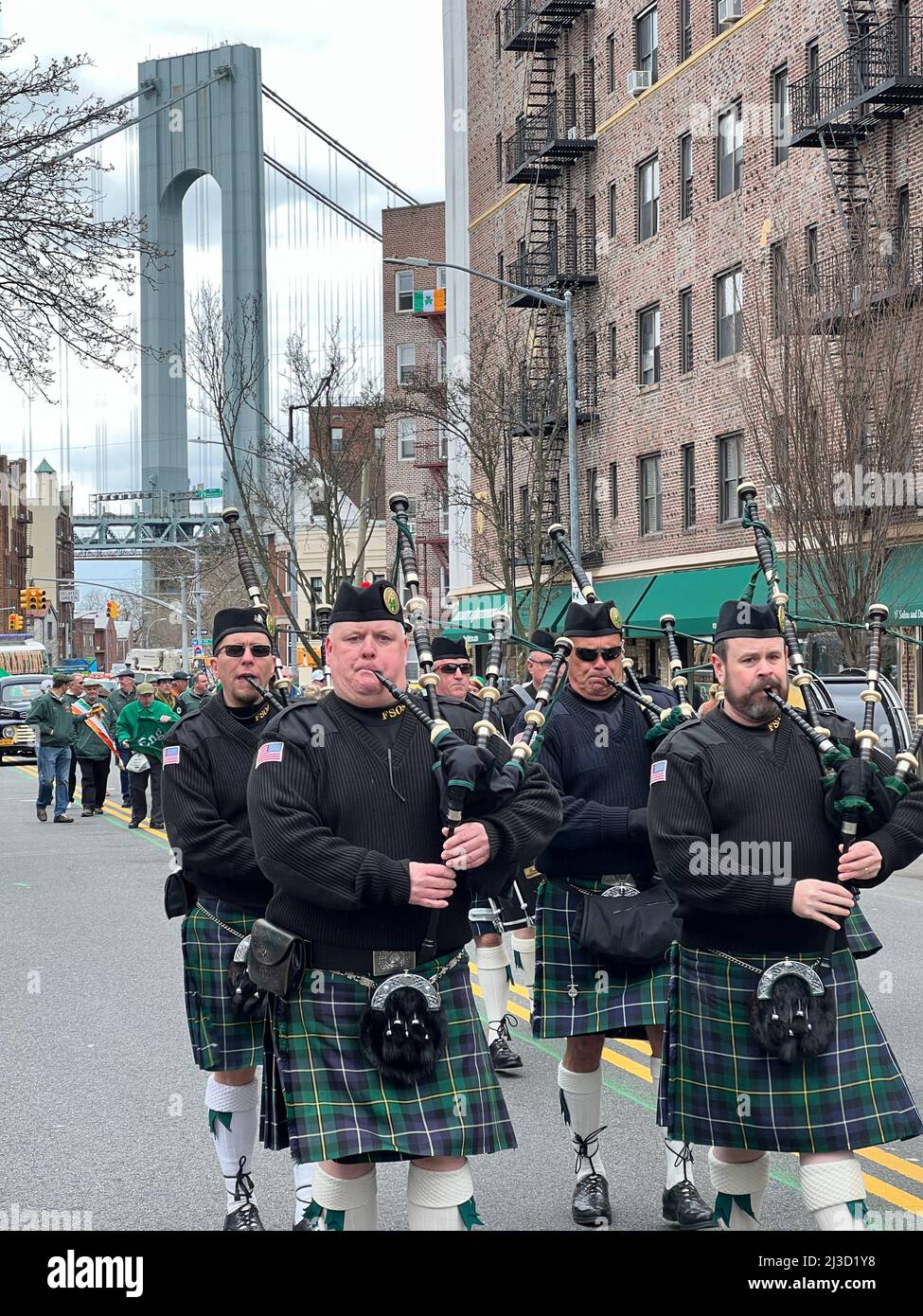 NYPD Emerald Society Pfeifen und Trommeln marschieren bei der Saint Patrick's Day Parade auf der 3. Avenue im Bay Ridge-Teil von Brooklyn, New York, mit einem Turm der Verrazano Bridge im Hintergrund. Stockfoto