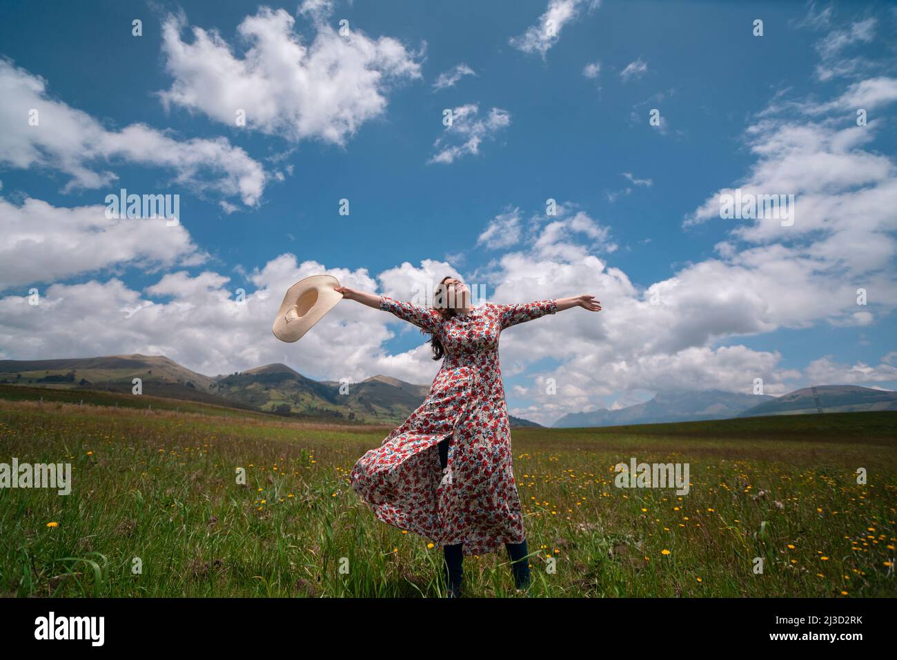 Schöne hispanische Frau allein mit geblümten Kleid und Hut heben ihre Arme und Kopf in einem Zeichen des Glücks in der Mitte eines Feldes während eines sonnigen Mo Stockfoto