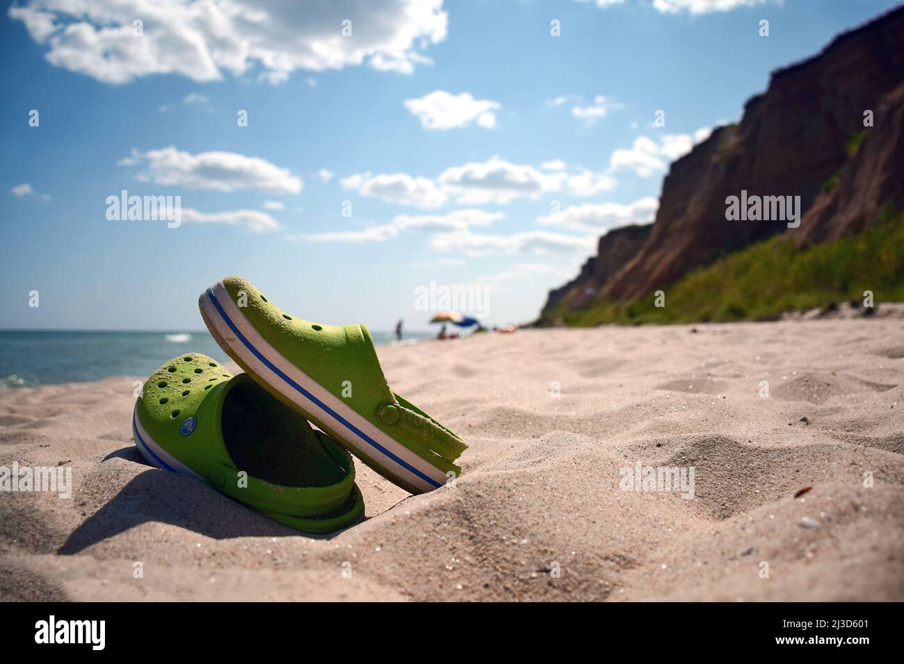 Im Vordergrund sind Sandalen an einem Sandstrand. Das Meer ist nicht sichtbar. Der Hintergrund ist verschwommen Stockfoto
