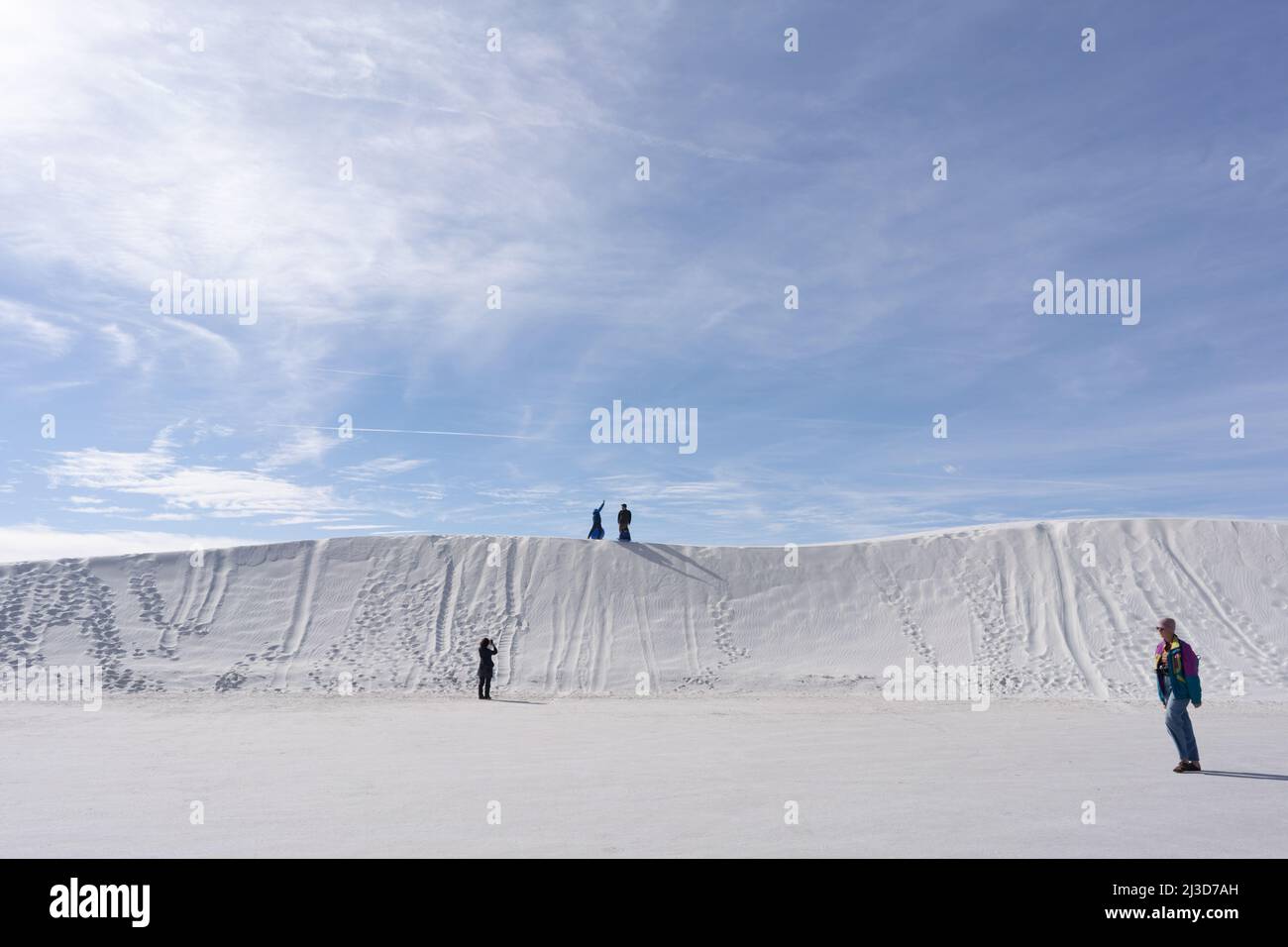 An einem sonnigen Tag vor einem großen blauen Himmel reiten die Menschen auf Untertassen durch die großen weißen Dünen aus Gips im White Sands National Park in New Mexico. Stockfoto